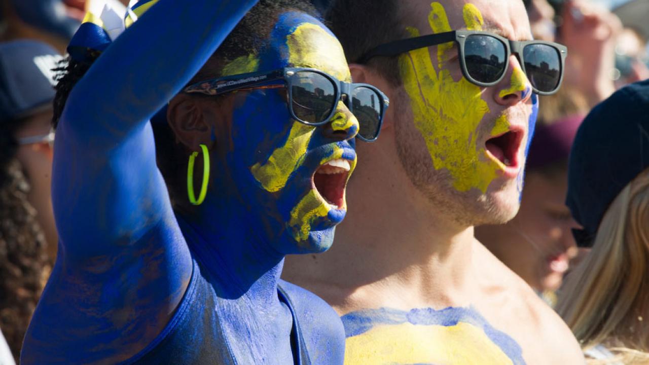 a male and female student painted in 澳门六合彩开奖结果走势图 blue and gold cheer on the Aggies at the annual homecoming football game